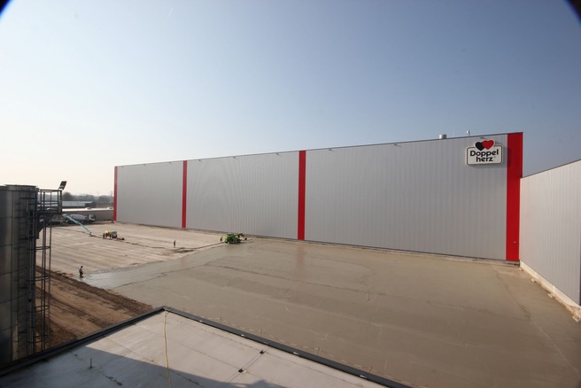 Aufbringen der Sauberkeitsschicht auf der Bodenplatte vor dem Queisser-Logistikzentrum mit Doppelherz-Logo, Arbeitsgeräte im Einsatz