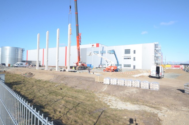 Bauarbeiten am Queisser-Logistikzentrum mit Hebekran, Arbeitsbühnen und errichteten Betonpfeilern vor dem Hauptgebäude.