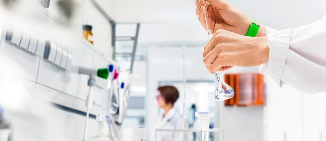 Hände halten einen Messkolben in einem Labor
