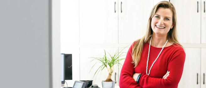 Frau im roten Pullover steht lächelnd im Büro