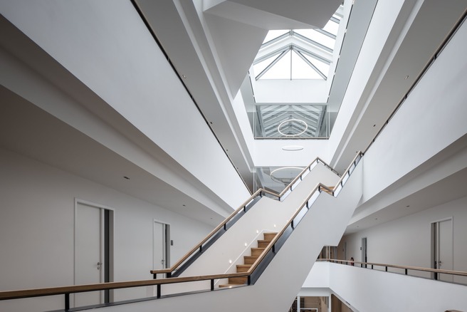 Atrium mit freitragender Treppe, weißem Geländer und Glasdach