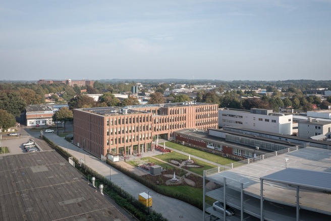 Luftaufnahme des Queisser-Campus mit modernem Verwaltungsgebäude, begrüntem Innenhof und Parkhaus im Vordergrund.