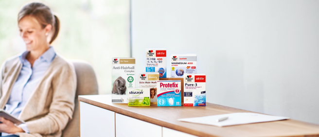 Queisser-Produkte auf einem Sideboard, im Hintergrund sitzt eine lächelnde Frau.